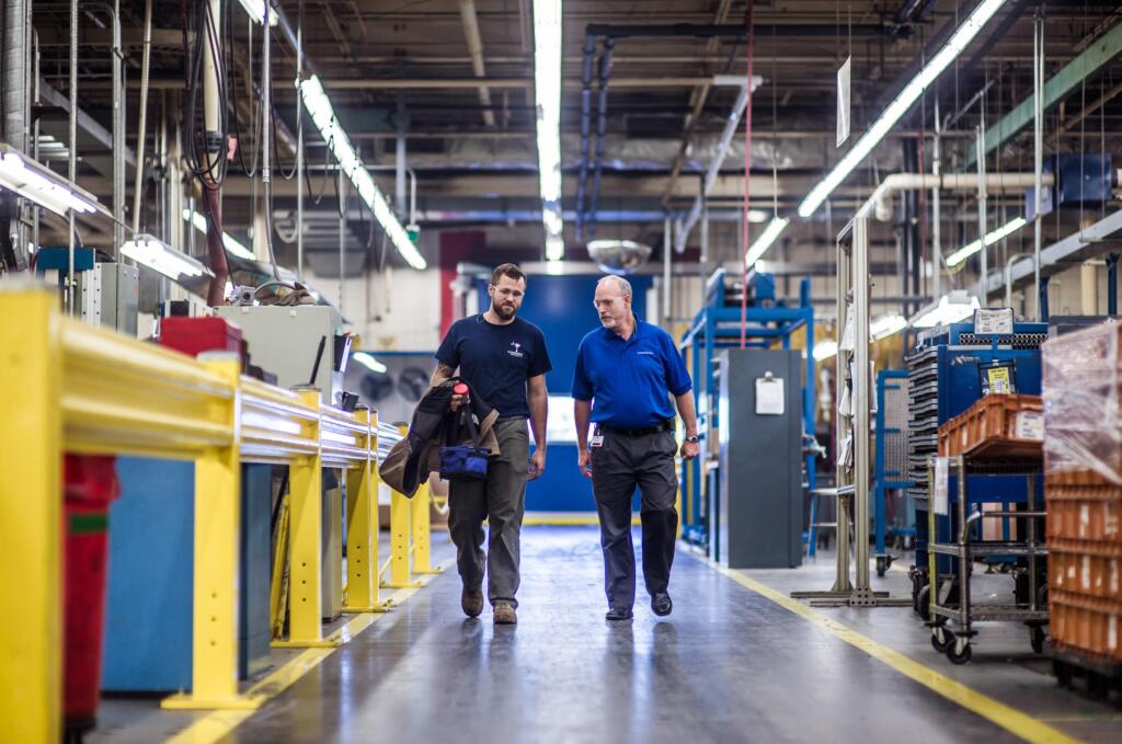 Employees Walking Through Facility Two men walking in the middle of the spacious room in an industrial building. There are machines on the both sides of them.